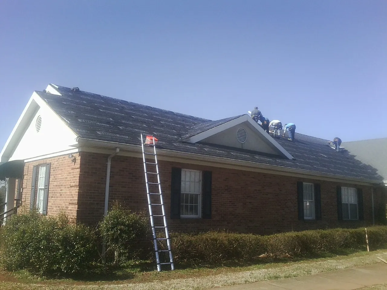 Crew tearing shingles off a brick ranch roof with a ladder set — Metal Roof Repair work by our crew in Bergen