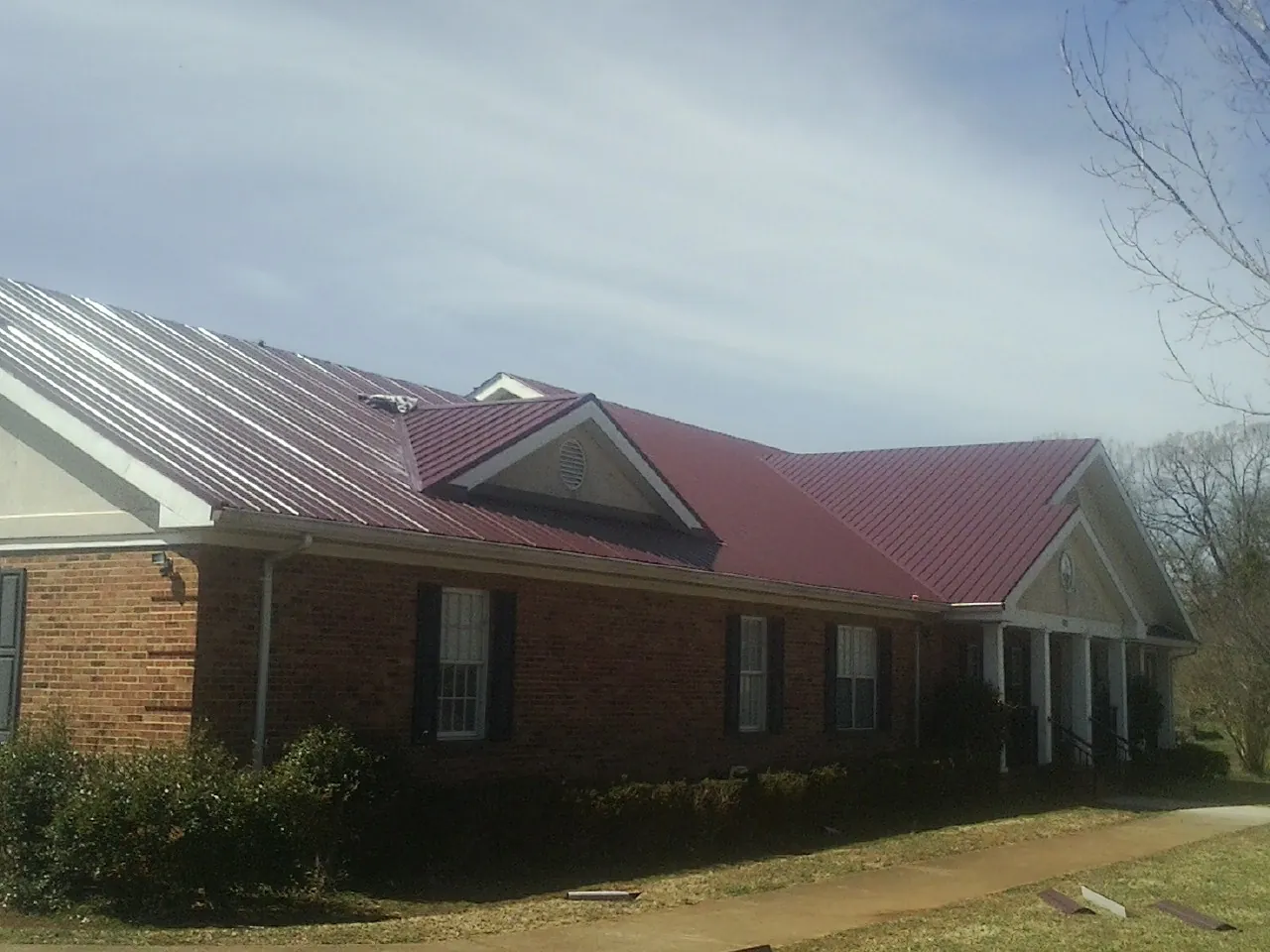 Red metal roof with gabled entries on a long brick building, from a Hail Damage Roof Repair job in Bergen