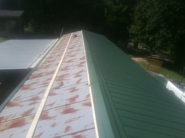 Old rusted panels beside newly installed green metal roofing — Wind Damage Roof Repair by Roofing Brothers in Bergen
