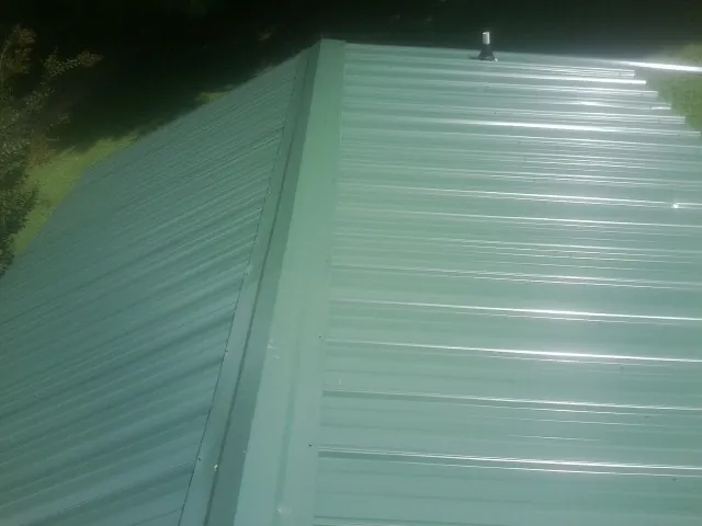 New green metal panels meeting at the ridge of a roof — Flat Roof Repair work by our crew in Bergen