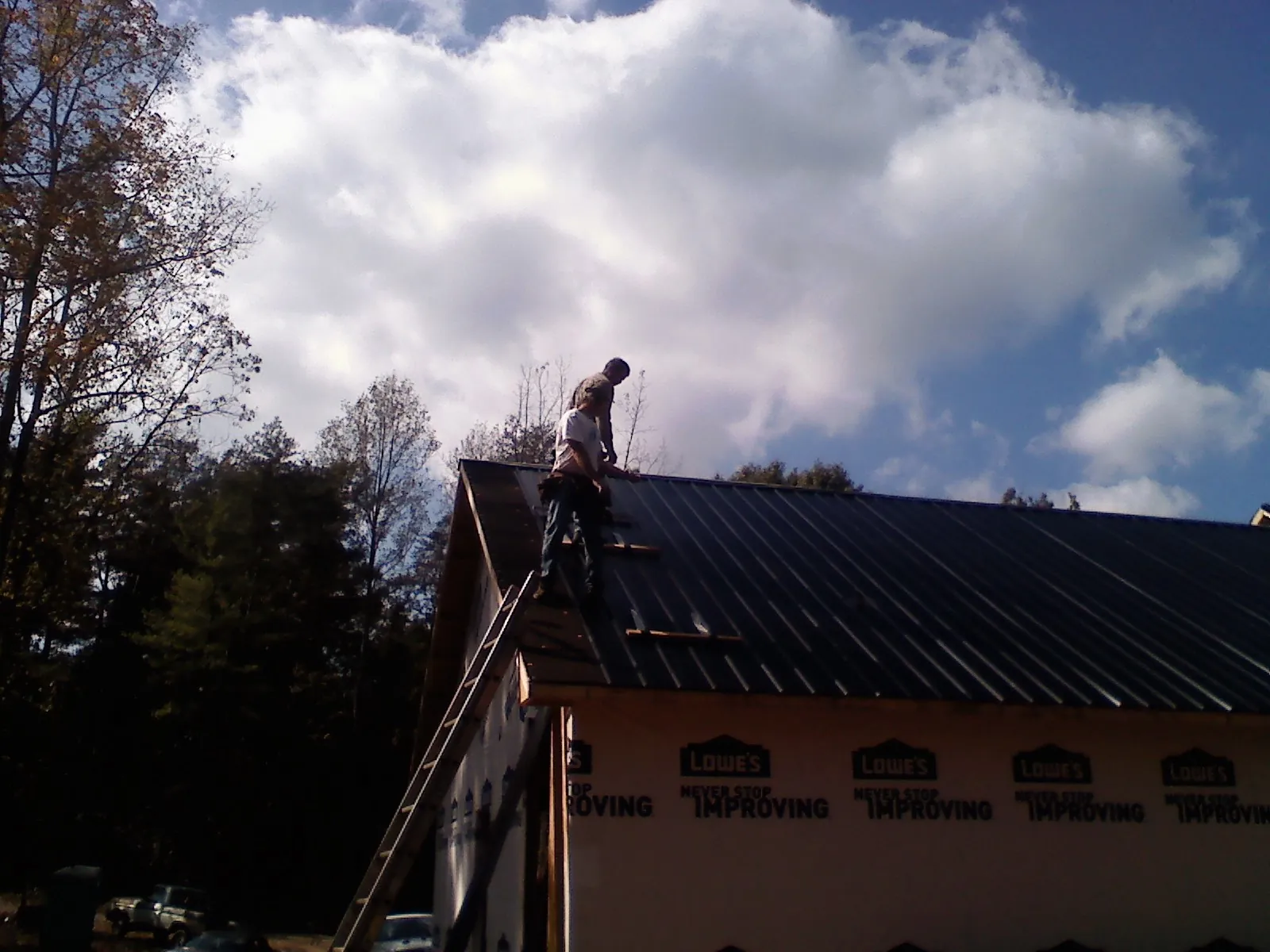 Roofer fastening dark metal panels high against a cloudy sky, from a Roof Inspection job in Bergen