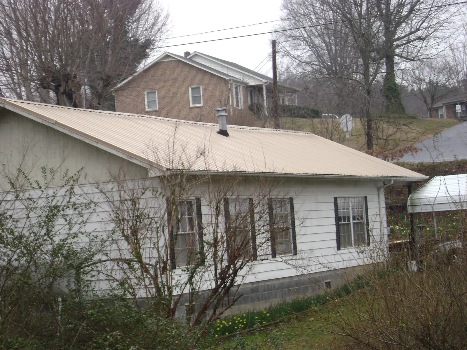 Tan metal roof on a white sided house set into a hillside — Commercial Roofing by Roofing Brothers in Bergen