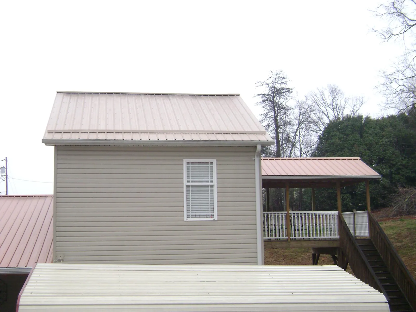 Tan metal roofs on a two story addition and attached porch, from a Roof Replacement job in Bergen